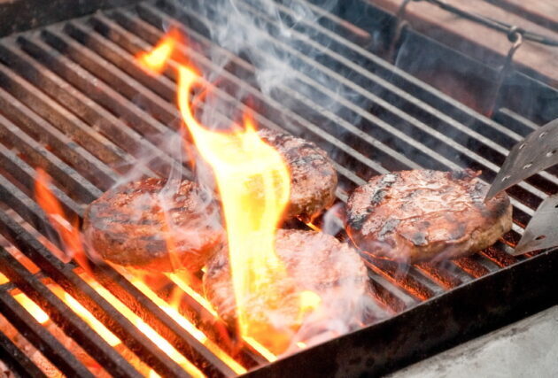 tasty burgers being cooked on a flaming barbecue